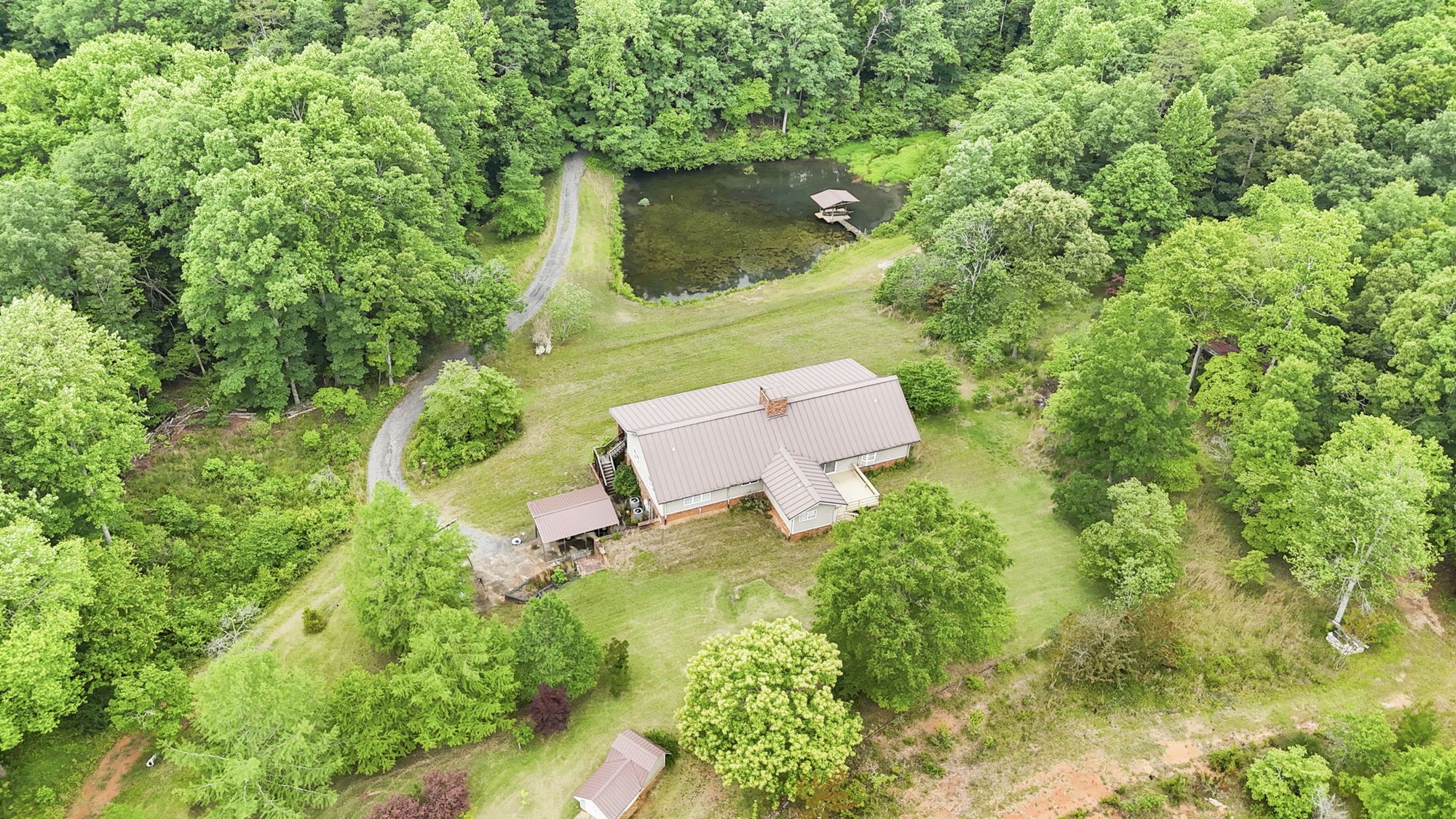 Aerial view of the 4454 Ledan Ext estate showing the main residence with red metal roof tucked into woodland and a small pond at the property edge